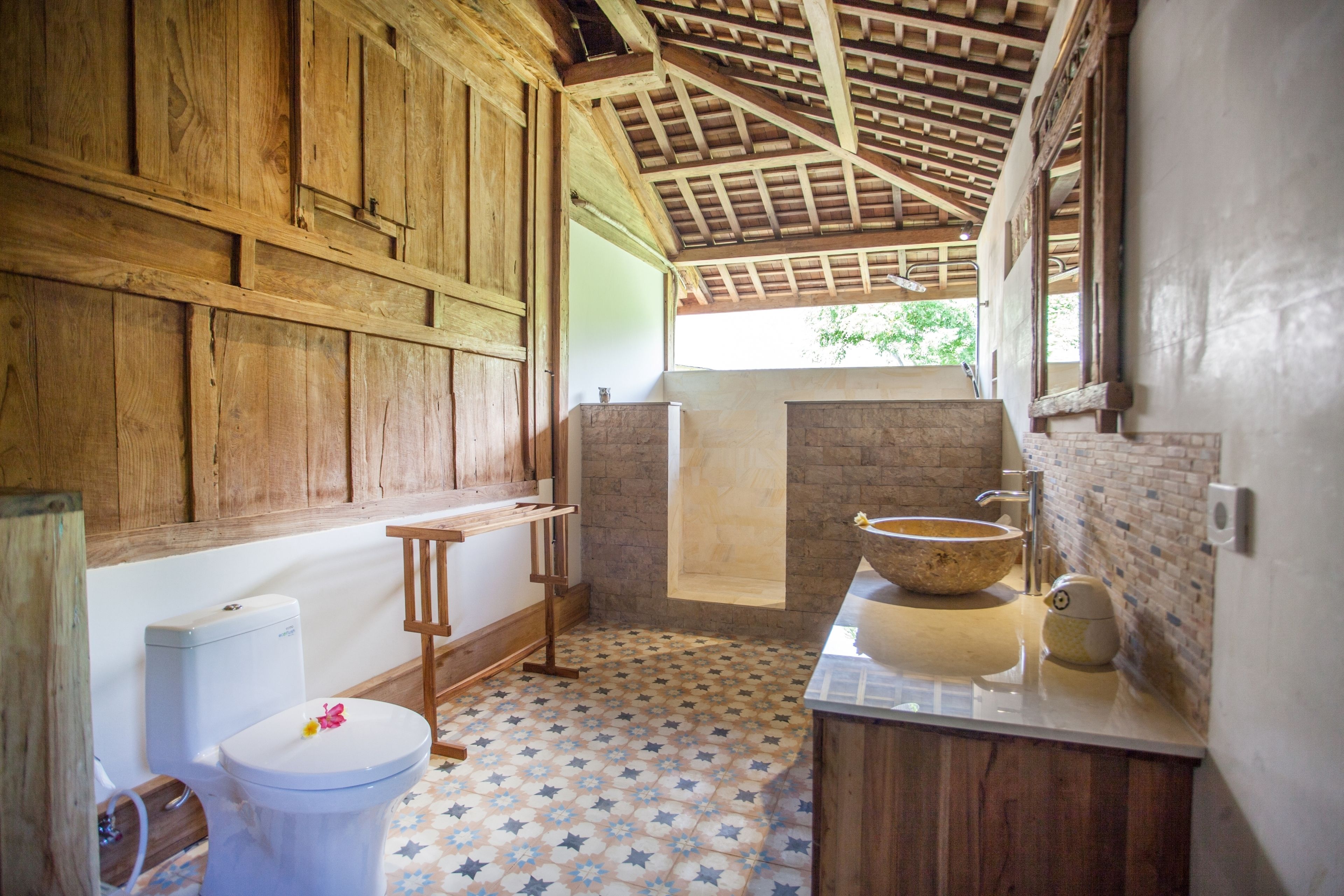 Une salle de bain rustique avec des murs en bois, un sol orné d’un motif en étoile, un grand lavabo en pierre et un banc en bois.