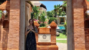 Una mujer está de pie en un arco de ladrillo con un letrero que dice 'SUN SUKO BOUTIQUE RETREAT'.