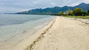 Una playa con agua cristalina, una orilla arenosa y montañas al fondo.