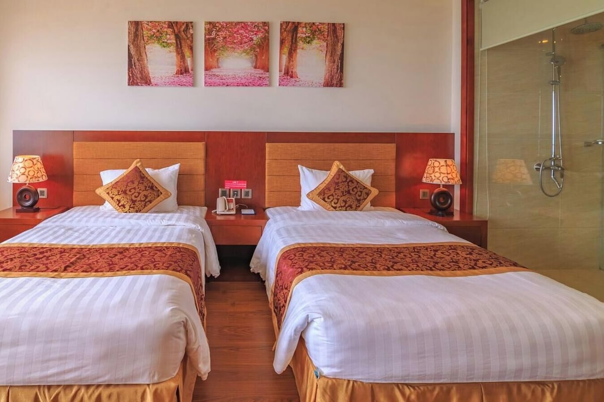 Habitación de hotel con dos camas, ducha y vistas a árboles.