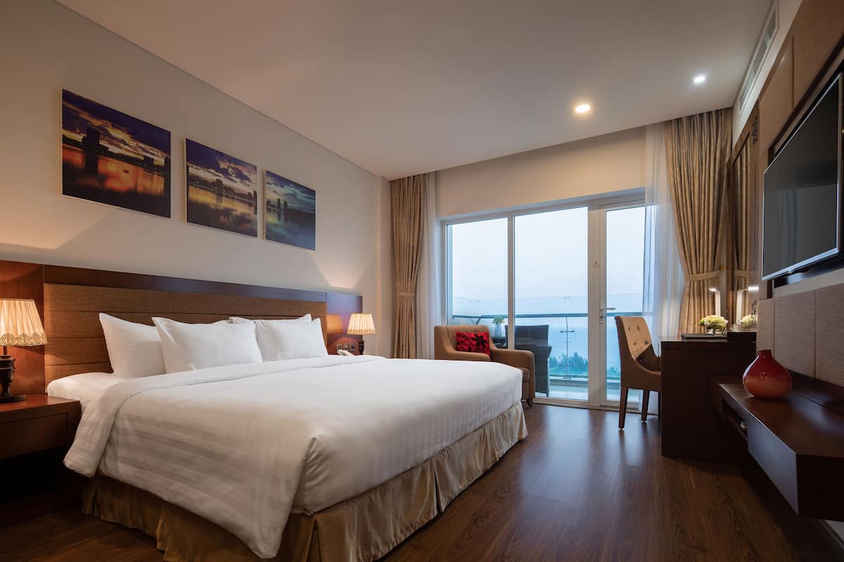 Une chambre d’hôtel avec un grand lit, un bureau, une chaise, une télévision et un balcon avec vue.