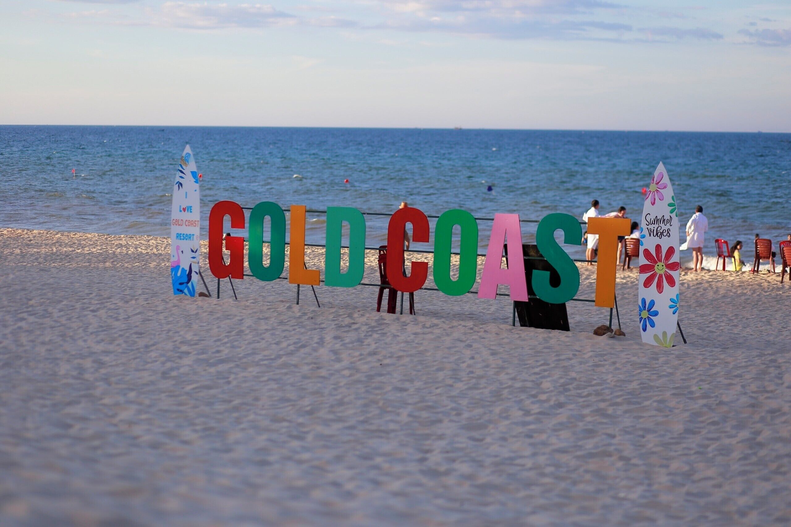 A beach with colorful letters spelling "GOLD COAST" and flags with text.