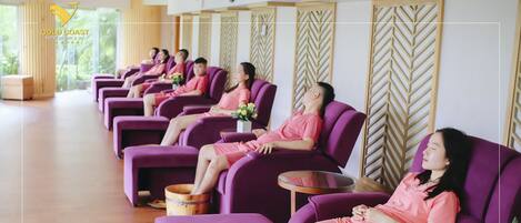 A row of purple massage chairs with wooden buckets, arranged in a spa area with a chevron-patterned wall and large windows.