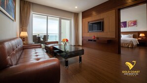 Een moderne hotelkamer met een leren bank, een glazen bijzettafeltje met bloemen, een aan de muur bevestigde televisie en een balkon met uitzicht.