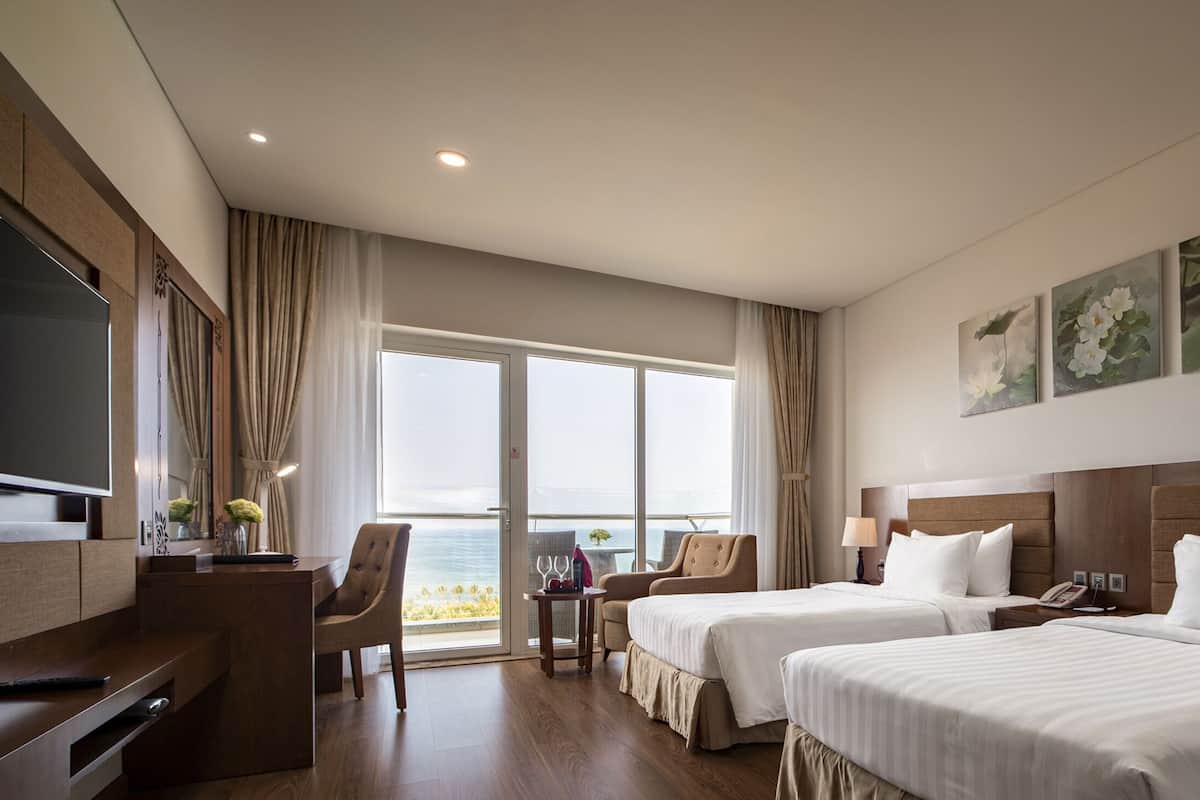 Une chambre d’hôtel avec deux lits, un bureau, une télévision et une vue sur l’océan.