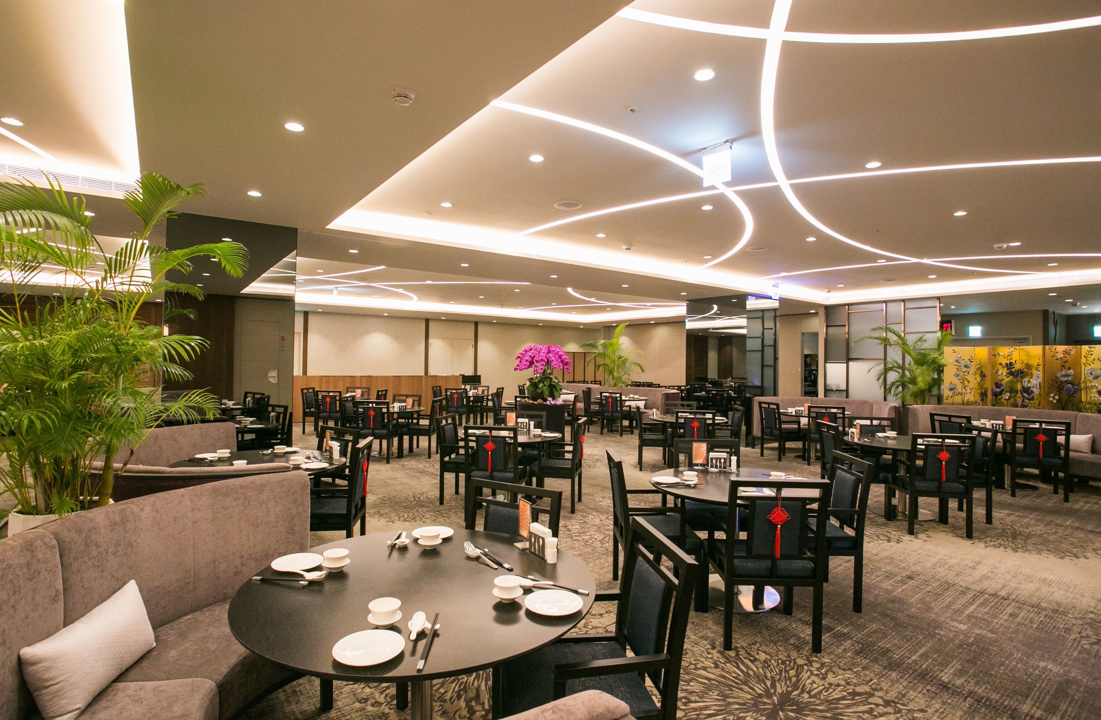 A spacious dining area with multiple tables and chairs, a central floral arrangement, and a modern ceiling design.