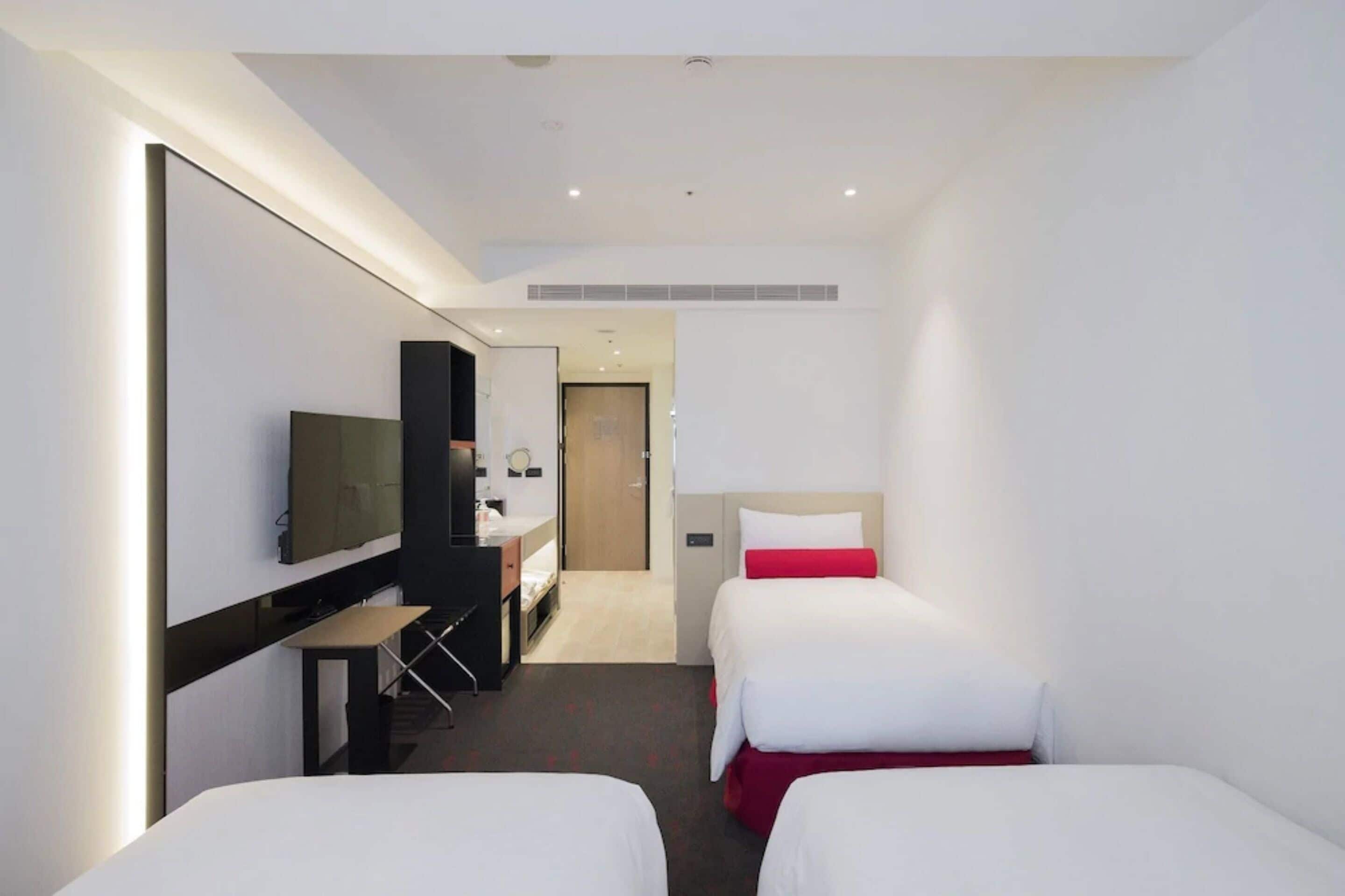 Habitación de hotel con dos camas, un escritorio, un televisor y un espejo.