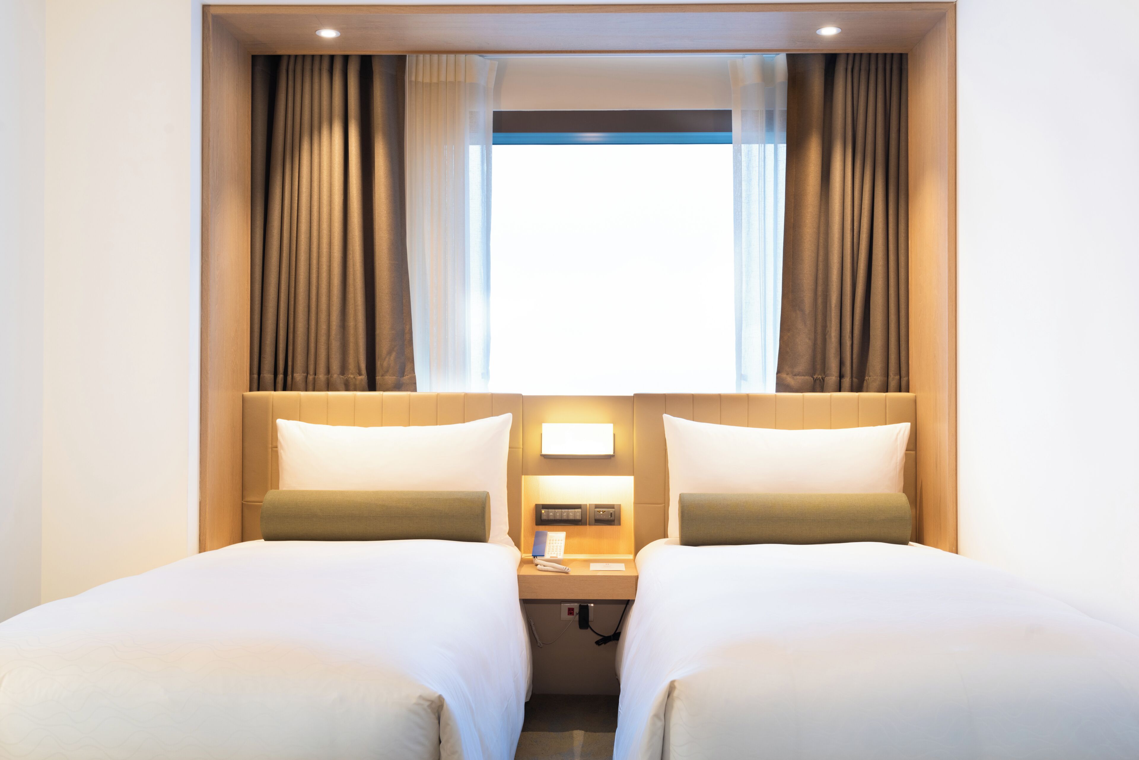 A hotel room with two beds, a nightstand with a phone, and a window with curtains.