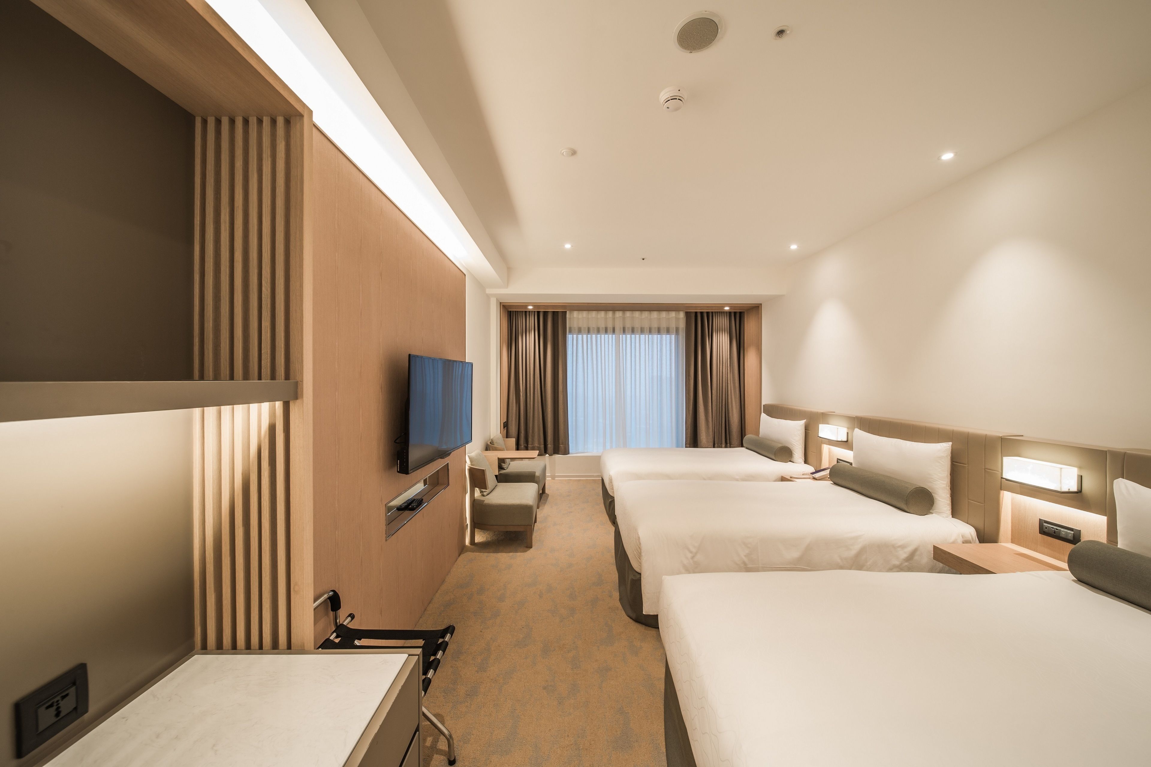 A hotel room with three beds, a TV, a desk, and a bathroom.