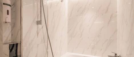 A modern bathroom with a glass-enclosed shower, a freestanding bathtub, and marble walls.