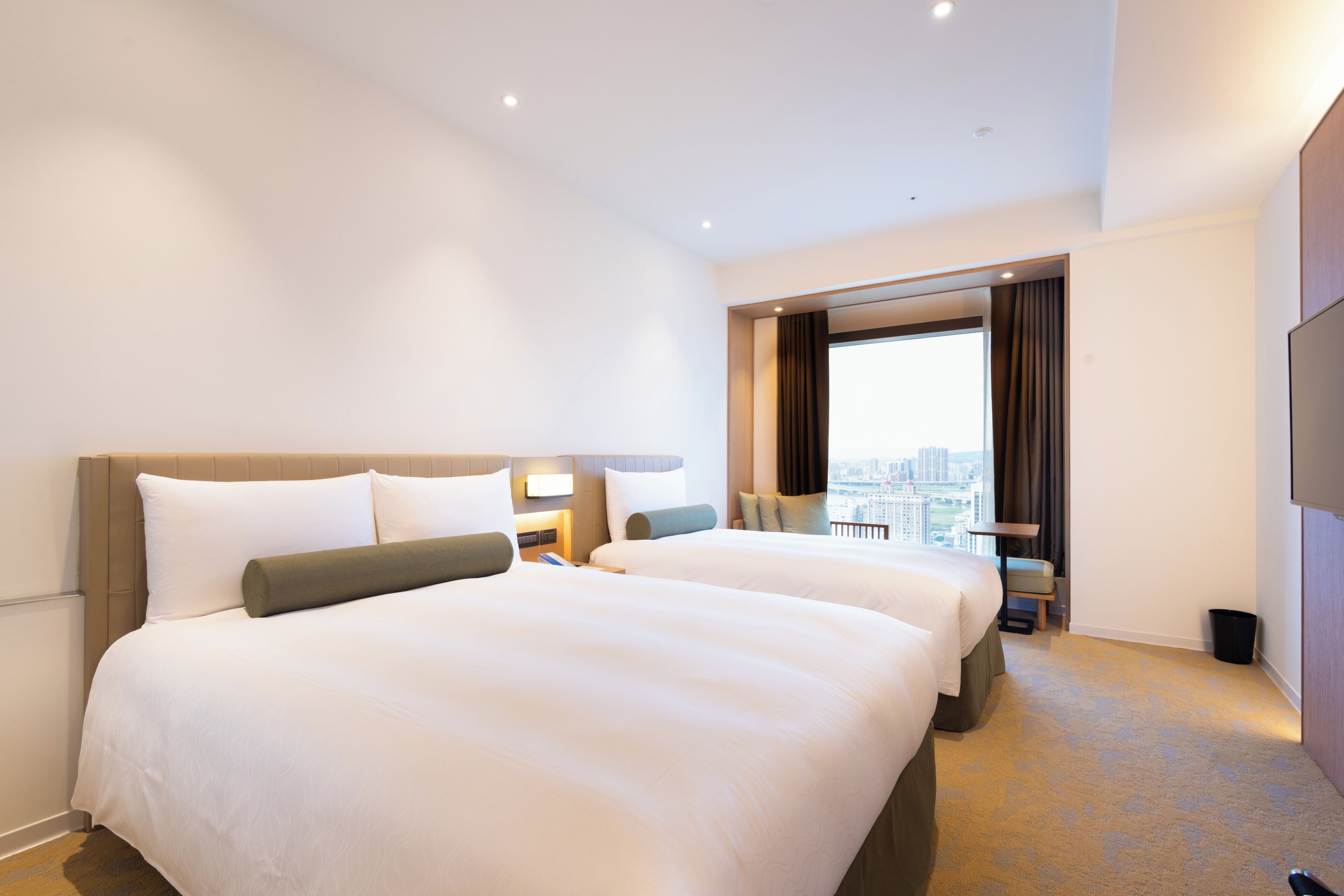 A hotel room with two beds, a city view, and a modern design.