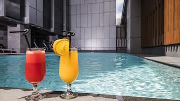 Duas bebidas junto a uma piscina, com um edifício moderno ao fundo.