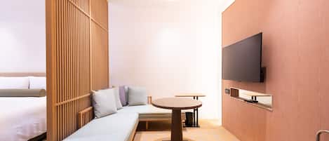 A modern hotel room with a sofa, a small round table, a TV mounted on the wall, and a chair.