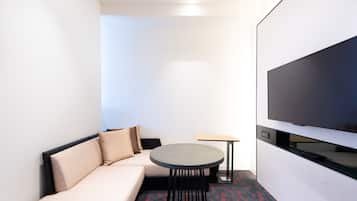 A compact hotel room with a sofa, a small round table, and a flat-screen TV mounted on the wall.