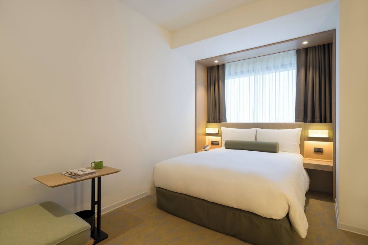 A hotel room with a bed, bedside tables, a small desk, and a chair.