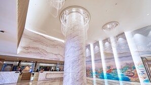 Un hall d’entrée orné de colonnes en marbre, un comptoir d’accueil et une fresque représentant un paysage tropical.