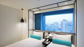 A modern hotel room with a large window, a bed, a bedside table, and a hanging light fixture.