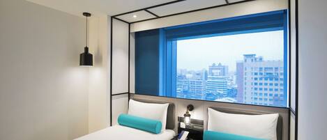 A modern hotel room with a large window, a bed, a bedside table, and a hanging light fixture.