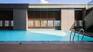 Une piscine dotée d’une terrasse en bois, de garde-corps en métal et offrant une vue sur les bâtiments en arrière-plan.