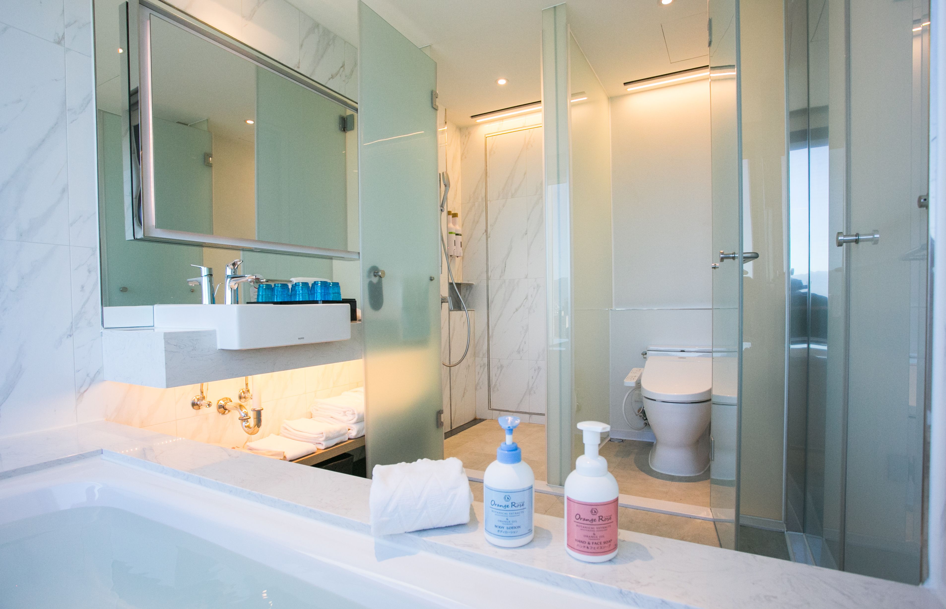 Een moderne badkamer met een marmeren wastafel, een grote spiegel, een douche met glazen wanden en een toilet.