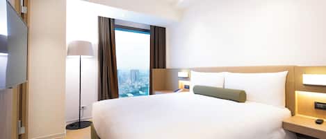 Habitación de hotel con una cama grande, un televisor de pantalla plana, una lámpara de pie y vistas a la ciudad.