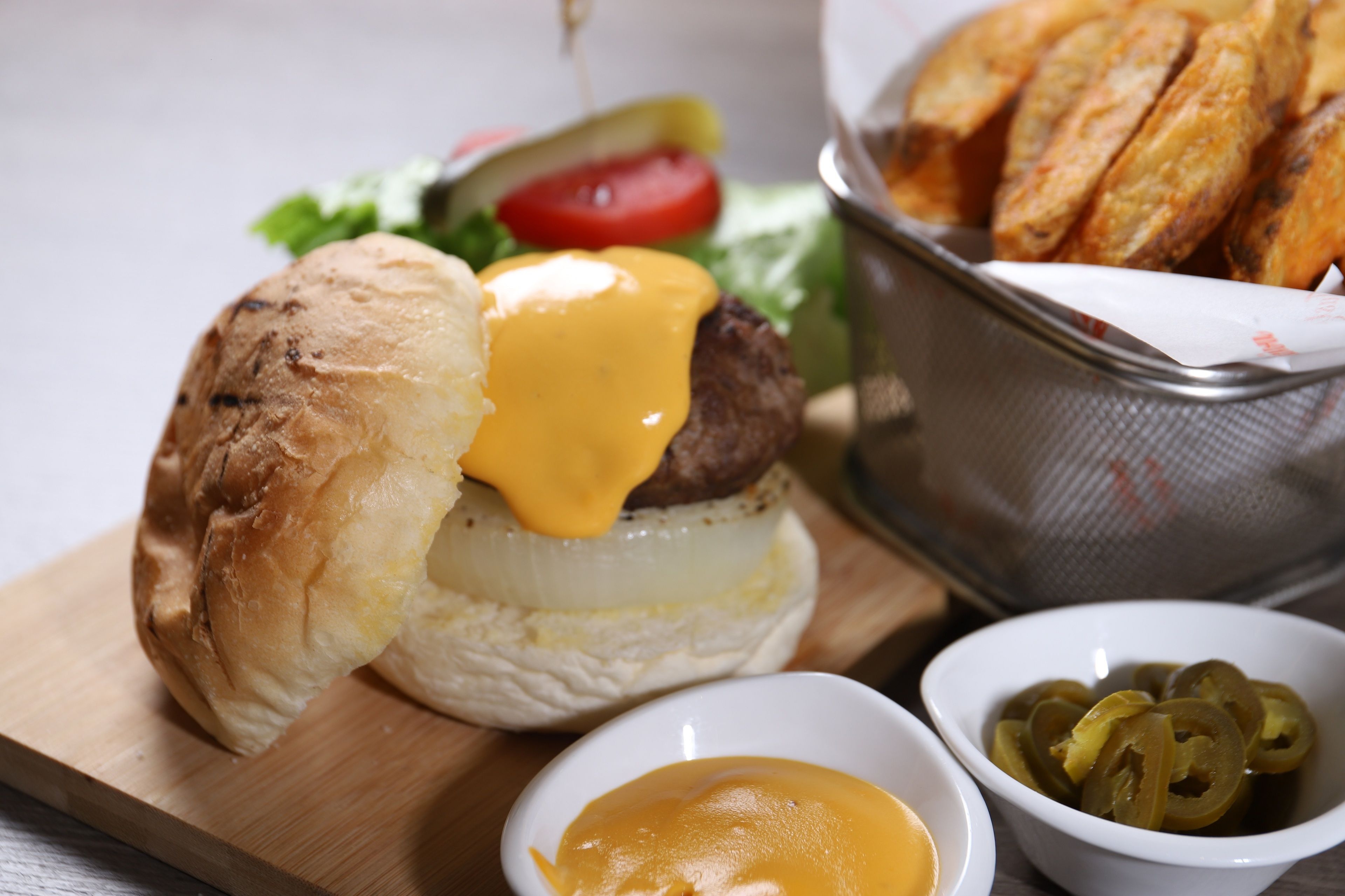 Ein Burger mit Käse, Salat und Tomate auf einem Brötchen, dazu eine Korb Pommes und zwei kleine Schalen mit Beilagen.