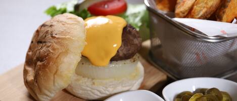 A burger with cheese, lettuce, and tomato on a bun, accompanied by a basket of fries and two small bowls of condiments.