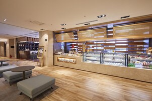 Een modern café met een houten toonbank, zitgedeelte en een vitrine vol gebak.