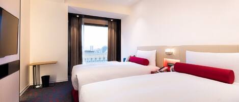 A hotel room with two beds, a TV, a desk, and a window with a city view.