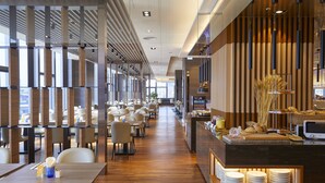 Un restaurant moderne avec des lambris en bois, un long comptoir où sont disposées des assiettes, et de nombreuses tables avec des chaises.