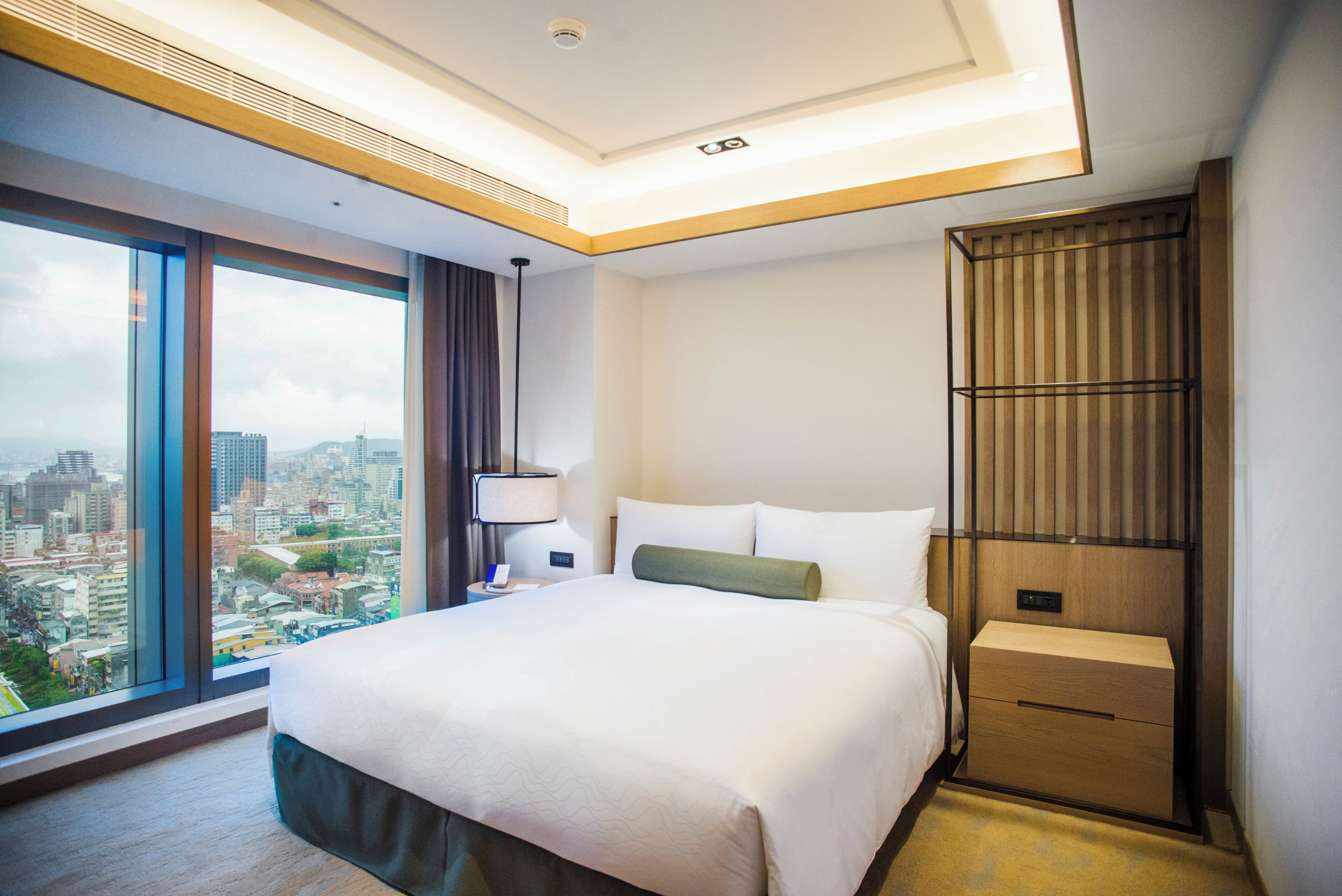 Camera d'albergo con un letto grande, un comodino, una lampada, una parete rivestita in legno e vista sulla città.