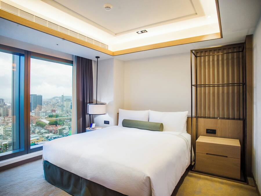 Camera d'albergo con un letto grande, un comodino, una lampada, una parete rivestita in legno e vista sulla città.
