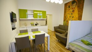 A modern kitchen with green cabinets, a dining table with chairs, a sofa, and a bed with striped bedding. - Klimt Apartments (Vienna)