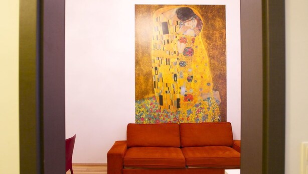 A modern living room with a wooden floor, a red sofa, and a large Gustav Klimt painting on the wall. - Klimt Apartments (Vienna)