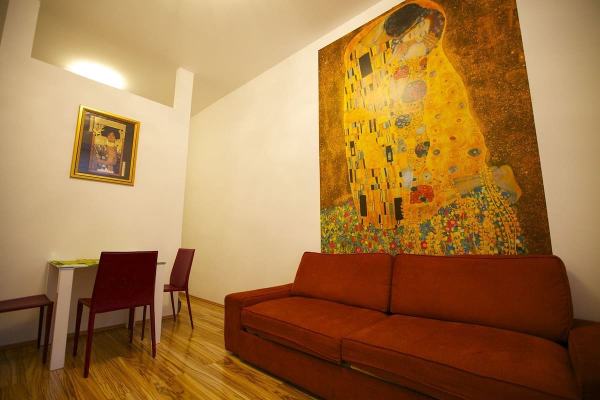 Ein Wohnzimmer mit einem großen Gemälde von Gustav Klimt, einem roten Sofa und einem Essbereich mit Stühlen und einem Tisch.