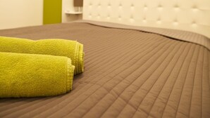 A hotel room with a brown quilted bedspread, two neatly folded yellow towels, a green door, and a white tufted headboard. - Klimt Apartments (Vienna)