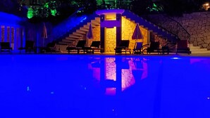 A nighttime swimming pool area with a stone wall and a staircase leading to a building. - Antas Deluxe Apartments (Fethiye)