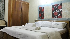 A neatly made bed with white linens and towels, a wooden wardrobe, and floral wall art. - Yaban Hotel (Abuja)