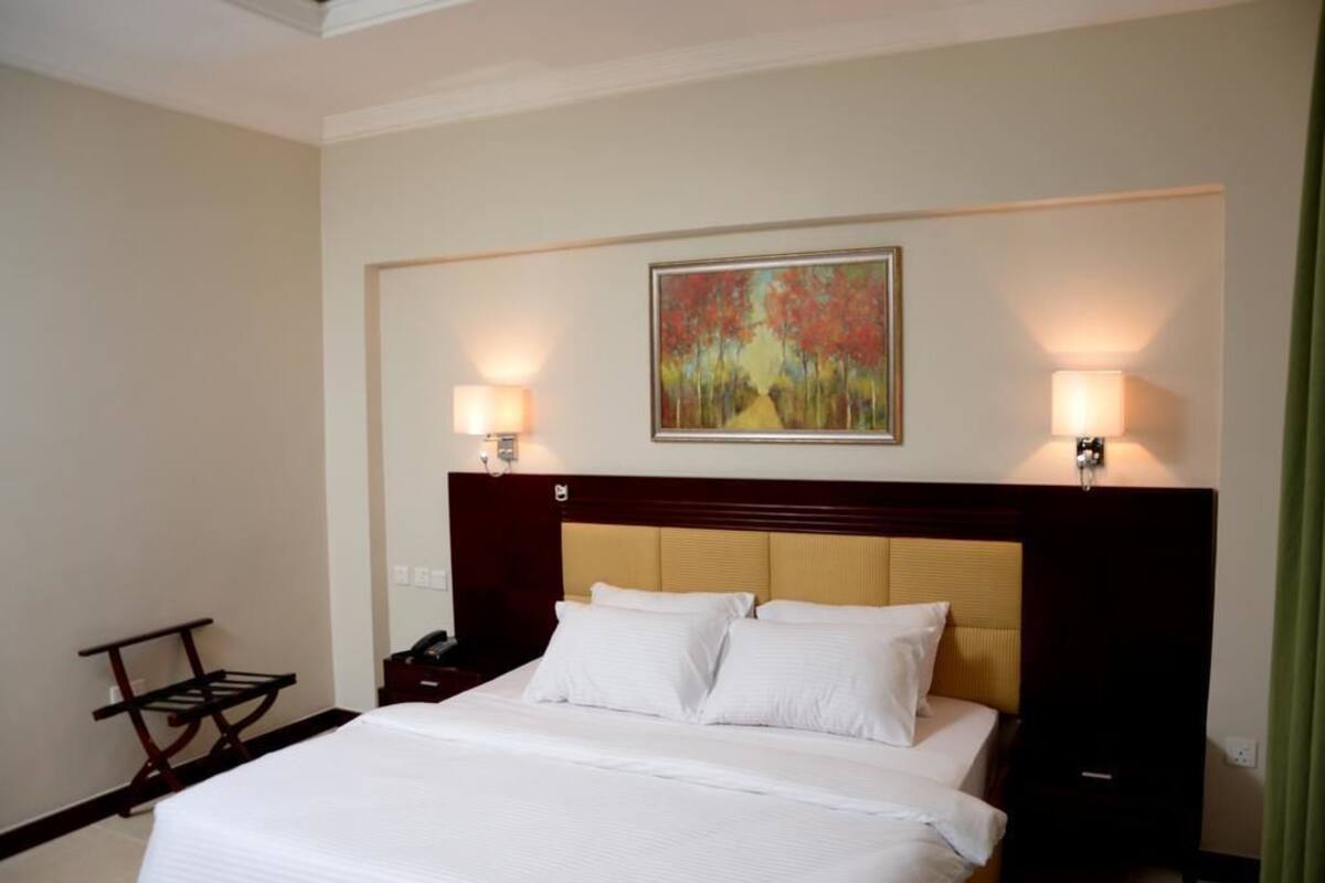 A hotel room with a large bed, two bedside lamps, a painting above the bed, and a nightstand with a phone.