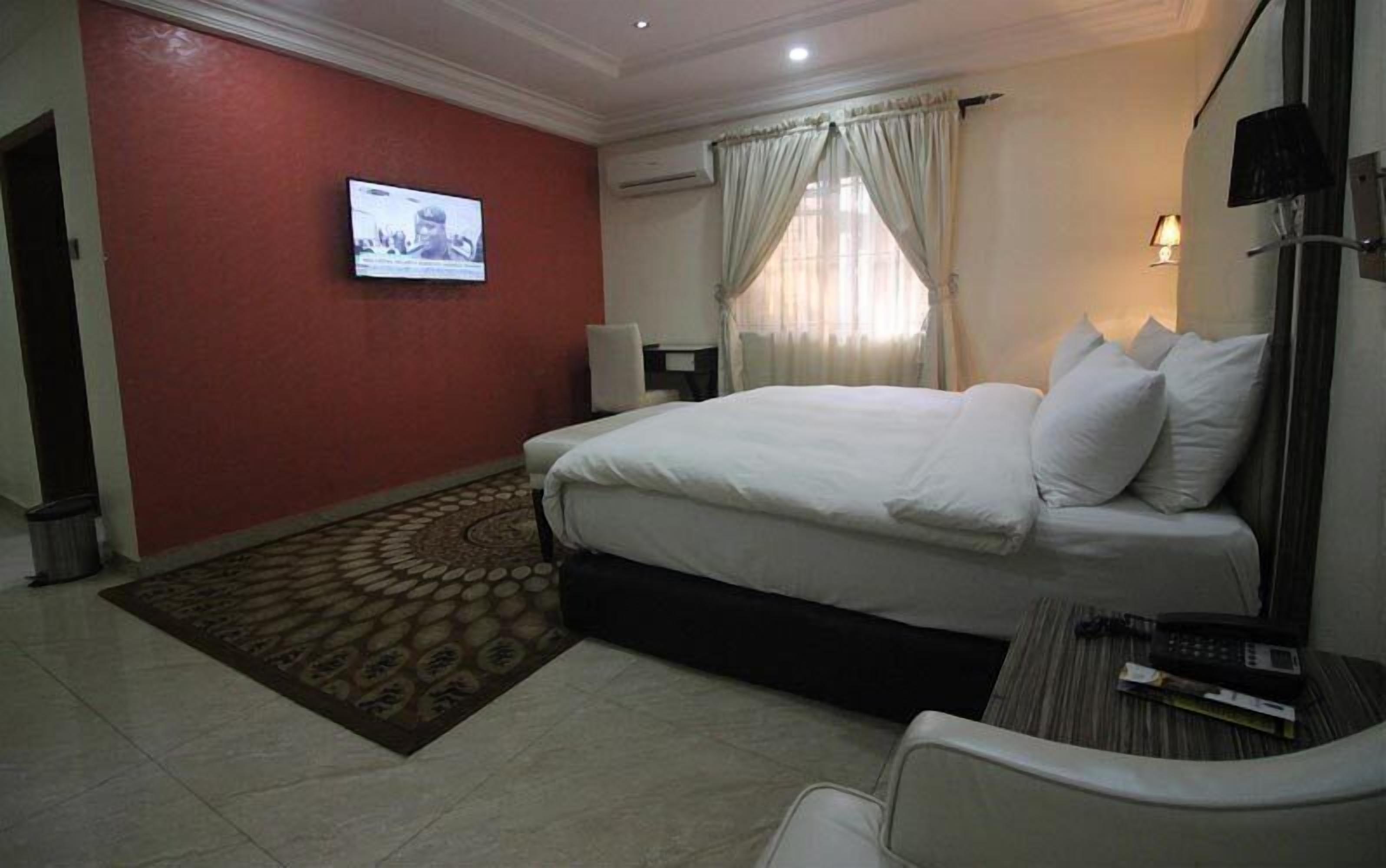 A hotel room with a bed, a television mounted on the wall, a desk with a chair, and a window with curtains.