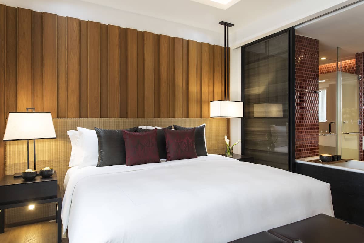 Une chambre d’hôtel avec un grand lit, deux tables de chevet avec des lampes, un mur revêtu de panneaux en bois et une cabine de douche en verre.