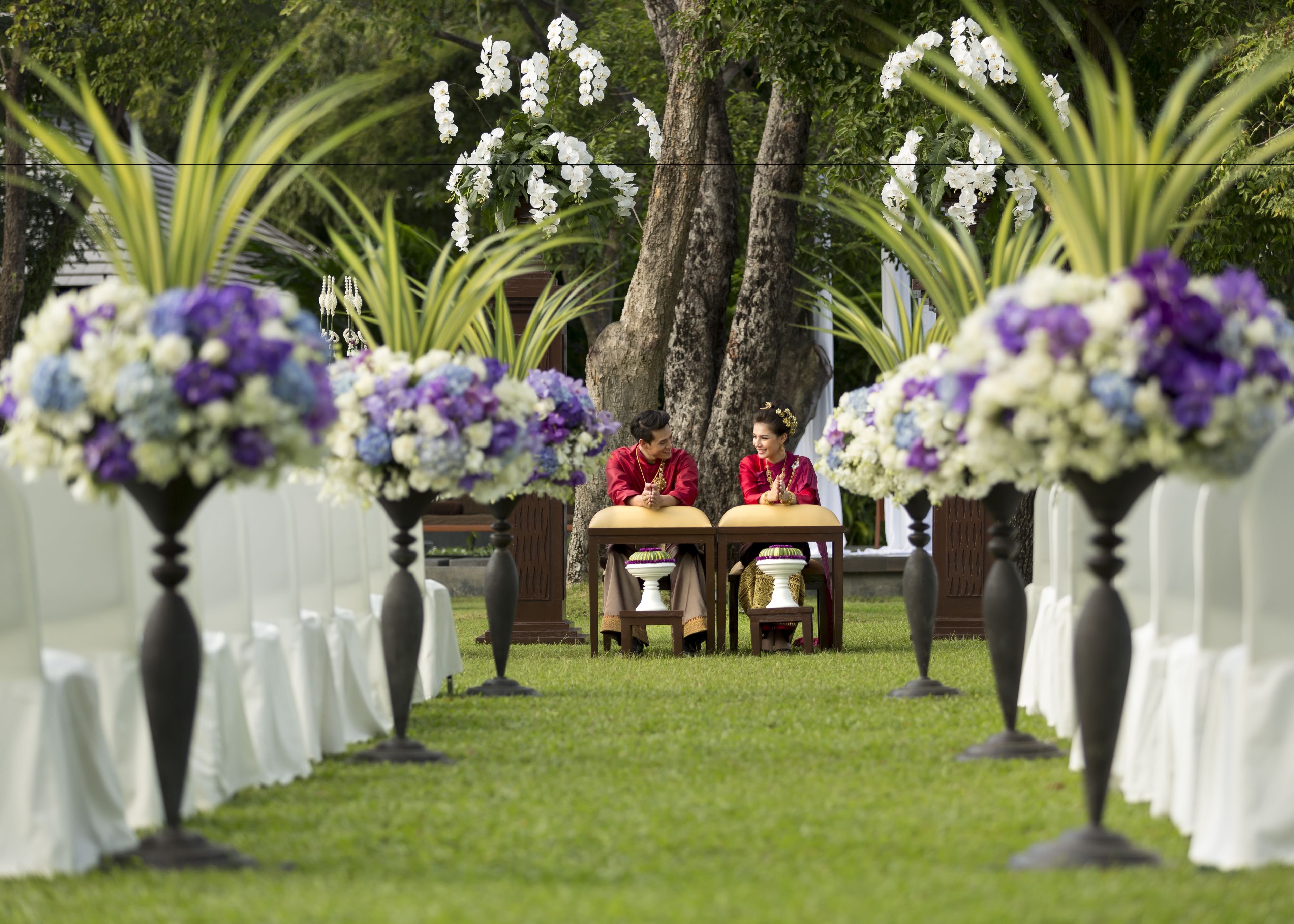 Un espacio ceremonial con dos personas sentadas en una mesa, rodeadas de sillas blancas y jarrones de flores.