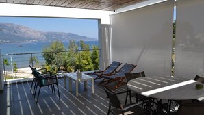 A balcony with a table and chairs, overlooking a body of water and hills. - K&K Luxury Beach Villas (Corfu)