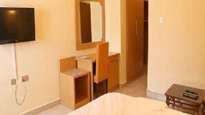 Una camera d'albergo con un letto, una scrivania, una sedia, una TV a parete e una porta che dà su un'altra stanza.