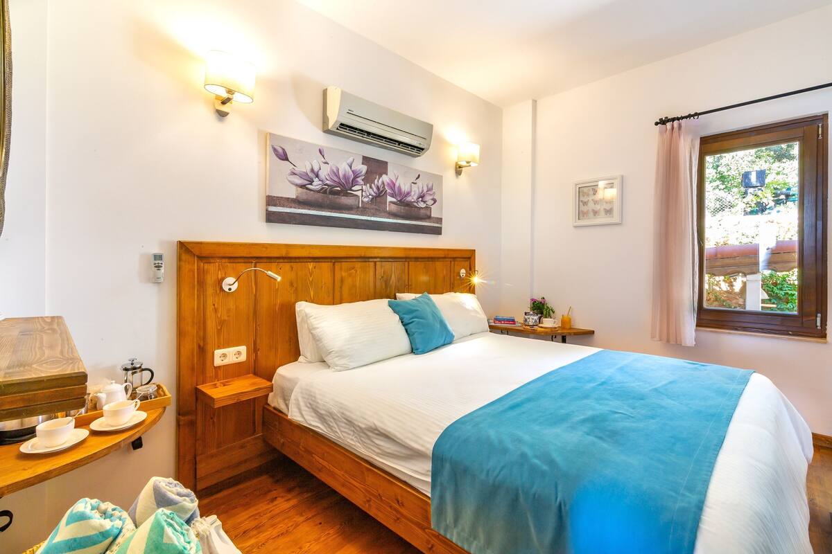 Une chambre à coucher avec un lit en bois, des tables de chevet, une commode, un appareil de climatisation, une fenêtre avec des rideaux et une lampe fixée au mur.