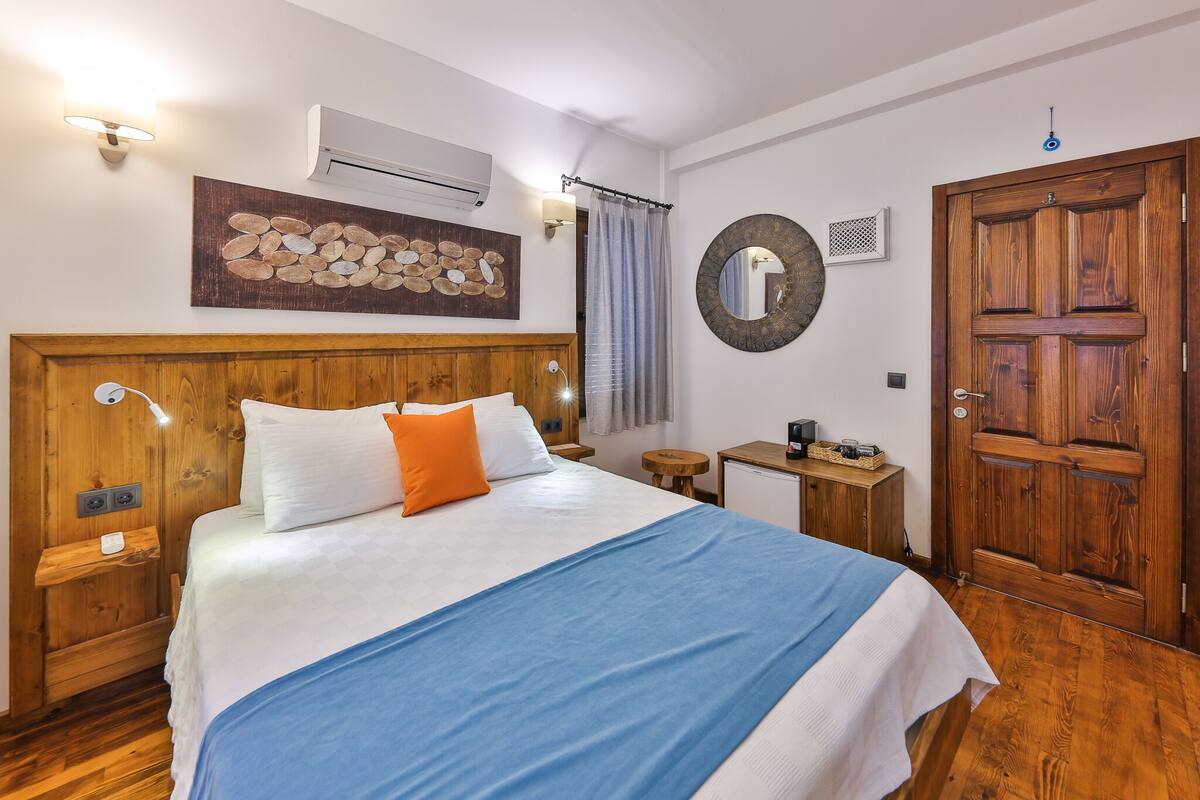 Une chambre à coucher avec une tête de lit en bois, un lit avec une literie blanche et bleue, une petite table de chevet avec une lampe, un miroir rond et une porte en bois.