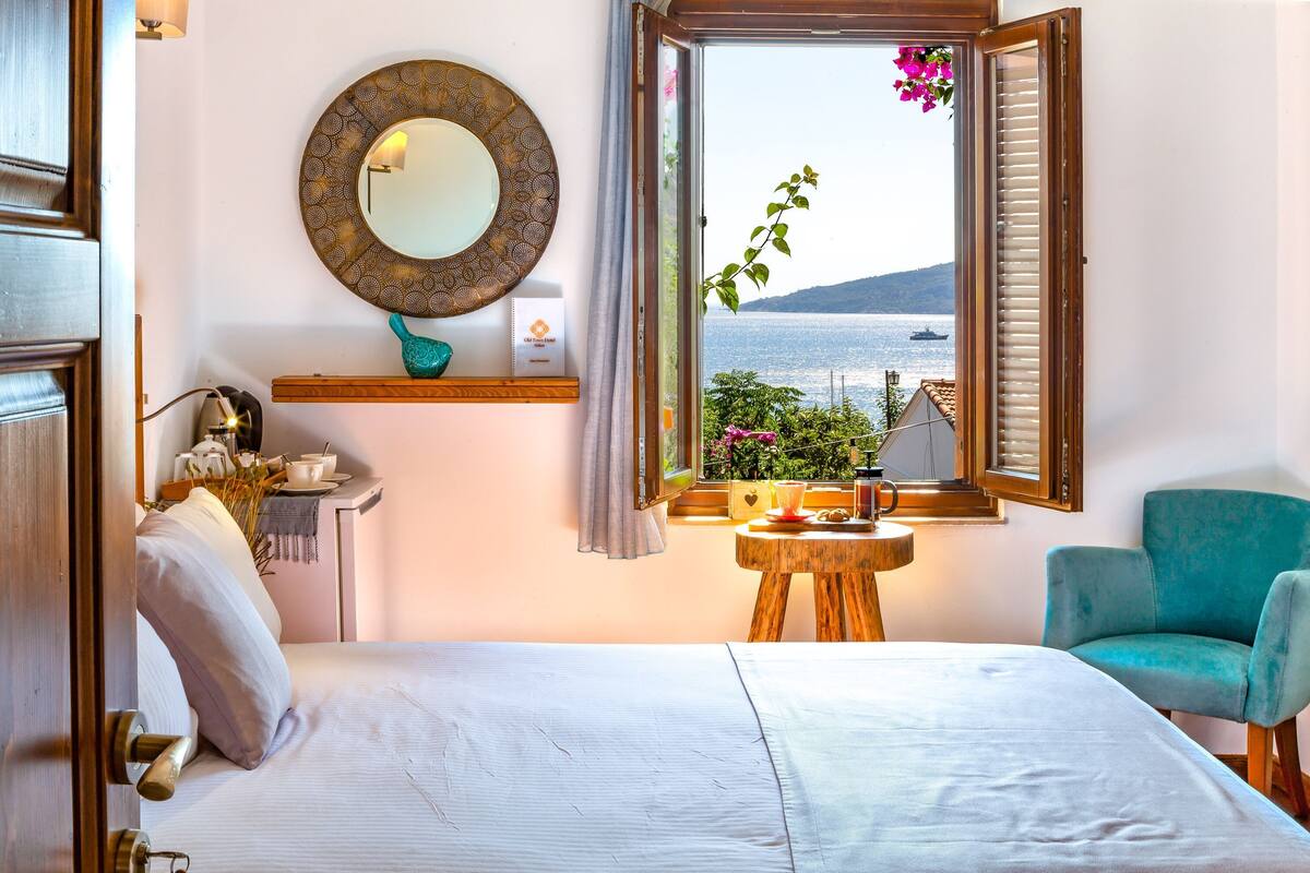 Une chambre à coucher avec un lit, une chaise, une petite table, une fenêtre donnant sur la mer et un miroir au mur.