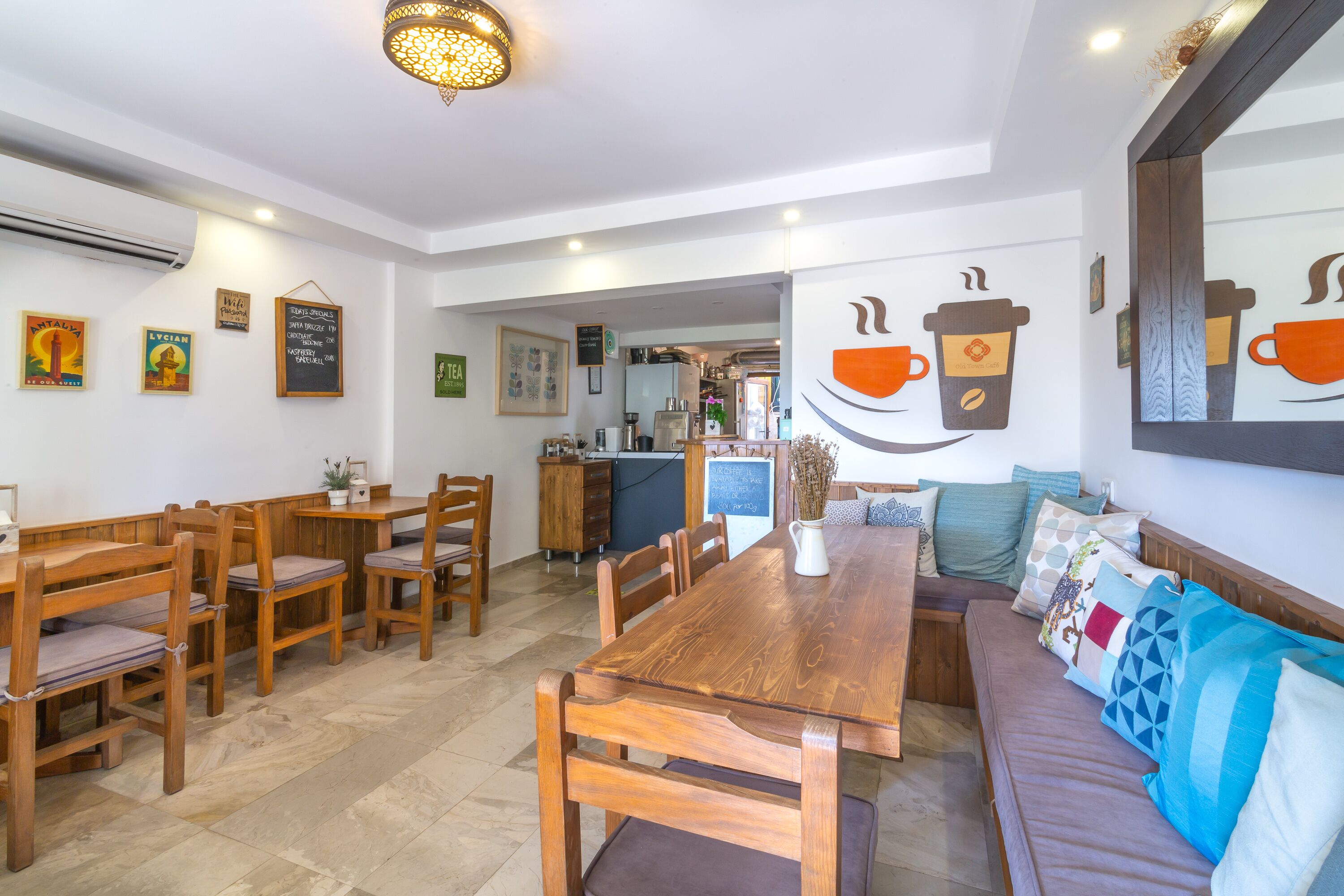 Un coin repas chaleureux, avec des meubles en bois, une décoration murale sur le thème du café et une cuisine ouverte visible au fond.