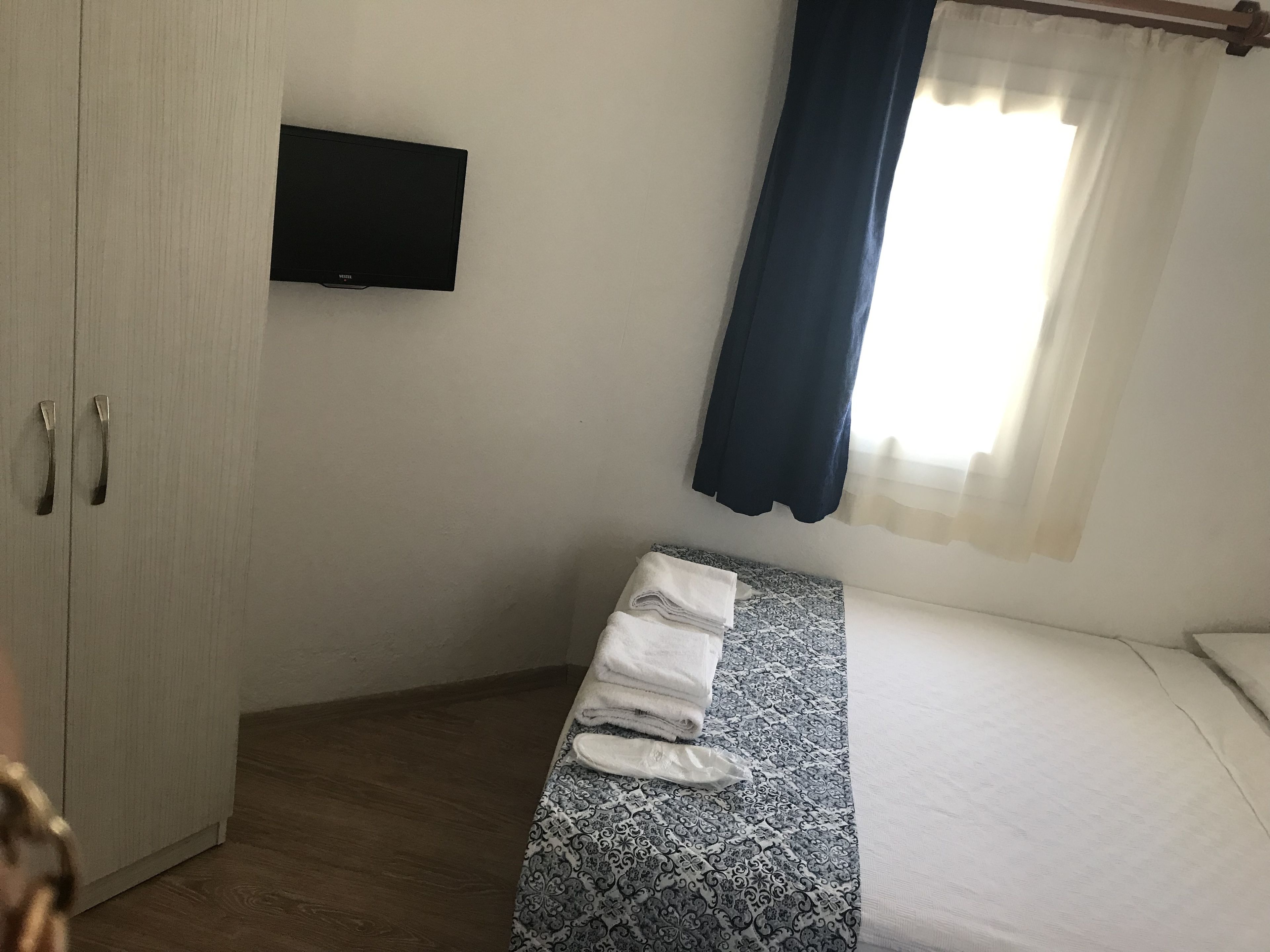 A bedroom with a bed, a TV mounted on the wall, a wardrobe, and a window with curtains.