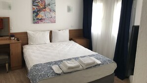 Une chambre d’hôtel avec un lit, un bureau, une chaise, un tableau au mur et une fenêtre avec des rideaux.